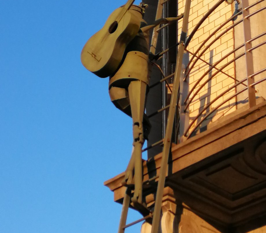 Romeo - Sculpture of a man with a guitar on his back climbing on a ladder景点图片