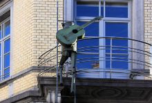 Romeo - Sculpture of a man with a guitar on his back climbing on a ladder景点图片
