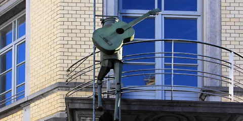 Romeo - Sculpture of a man with a guitar on his back climbing on a ladder