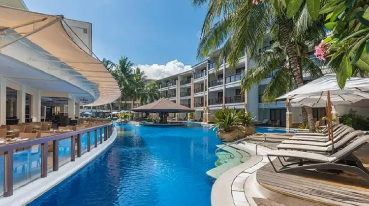 Outdoor swimming pool surrounded by greenery and equipped with comfortable lounge chairs at Henann Lagoon Resort