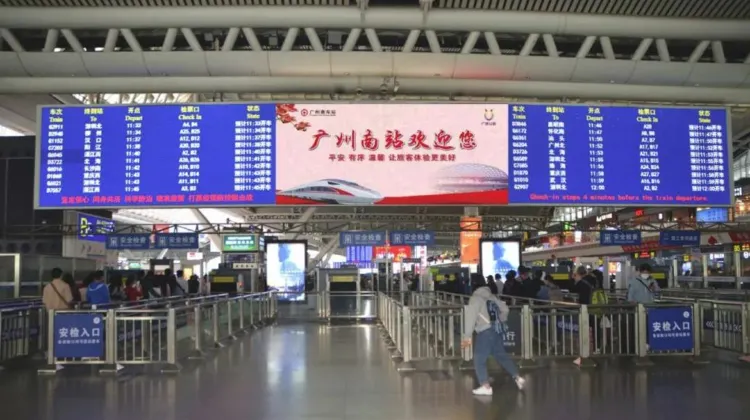広州南駅の構内。電光掲示板に発車時刻と列車番号が表示され、改札口前に多くの旅行者が並ぶ様子。