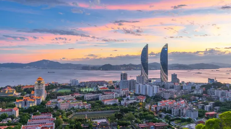 夕暮れの厦門市街。海辺に並ぶビル群と特徴的なツインタワーが夕焼け空に映える風景。