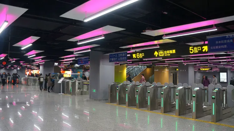 上海駅の地下鉄改札口。ピンク色の照明が印象的な構内で、5番出口・6番出口の案内表示が見える。